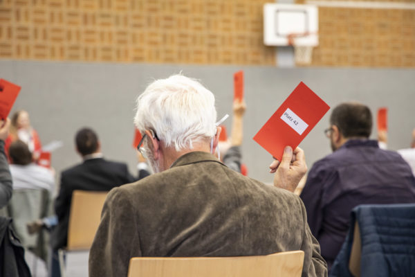 Ansicht von hintern: sitzendes PArteimitglied mit Wahlkarte
